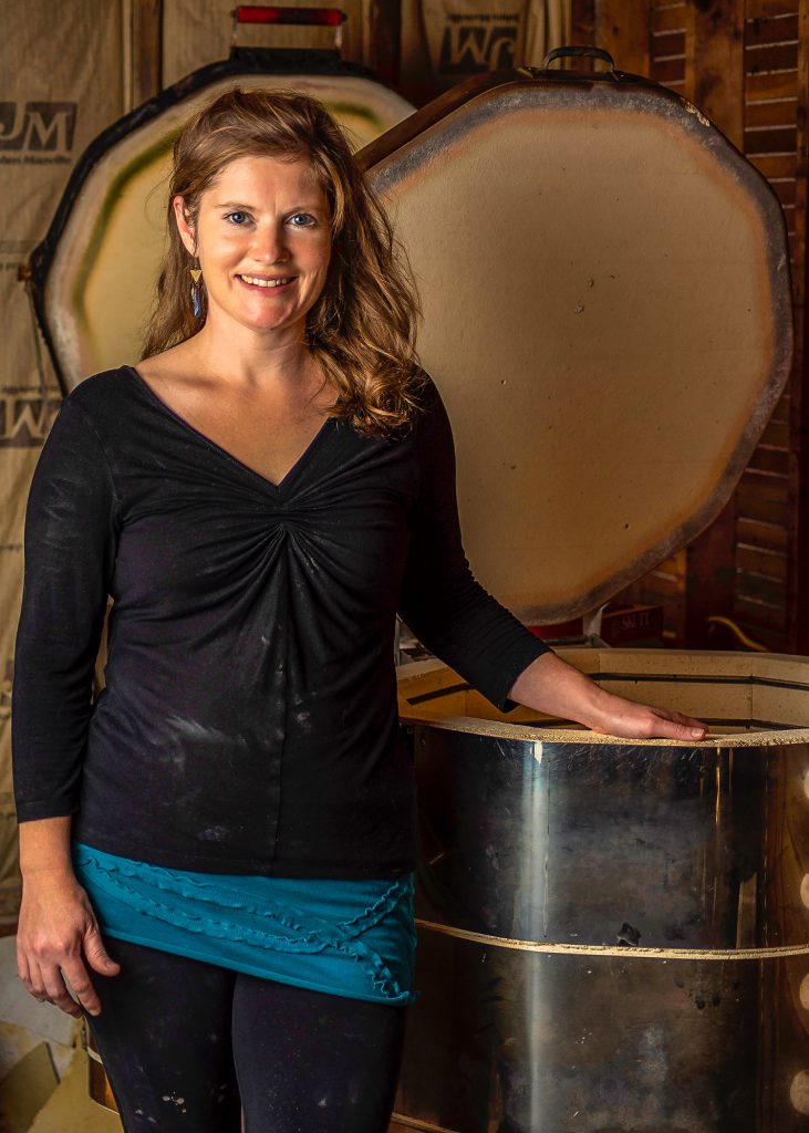 Amy Mason, potter, standing beside her kiln